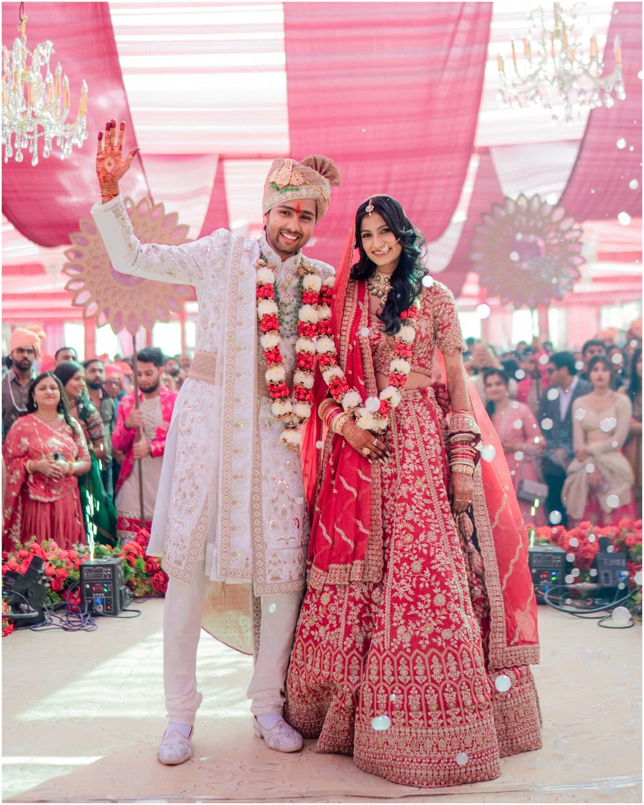 A newlywed couple celebrating under a pink wedding mandap