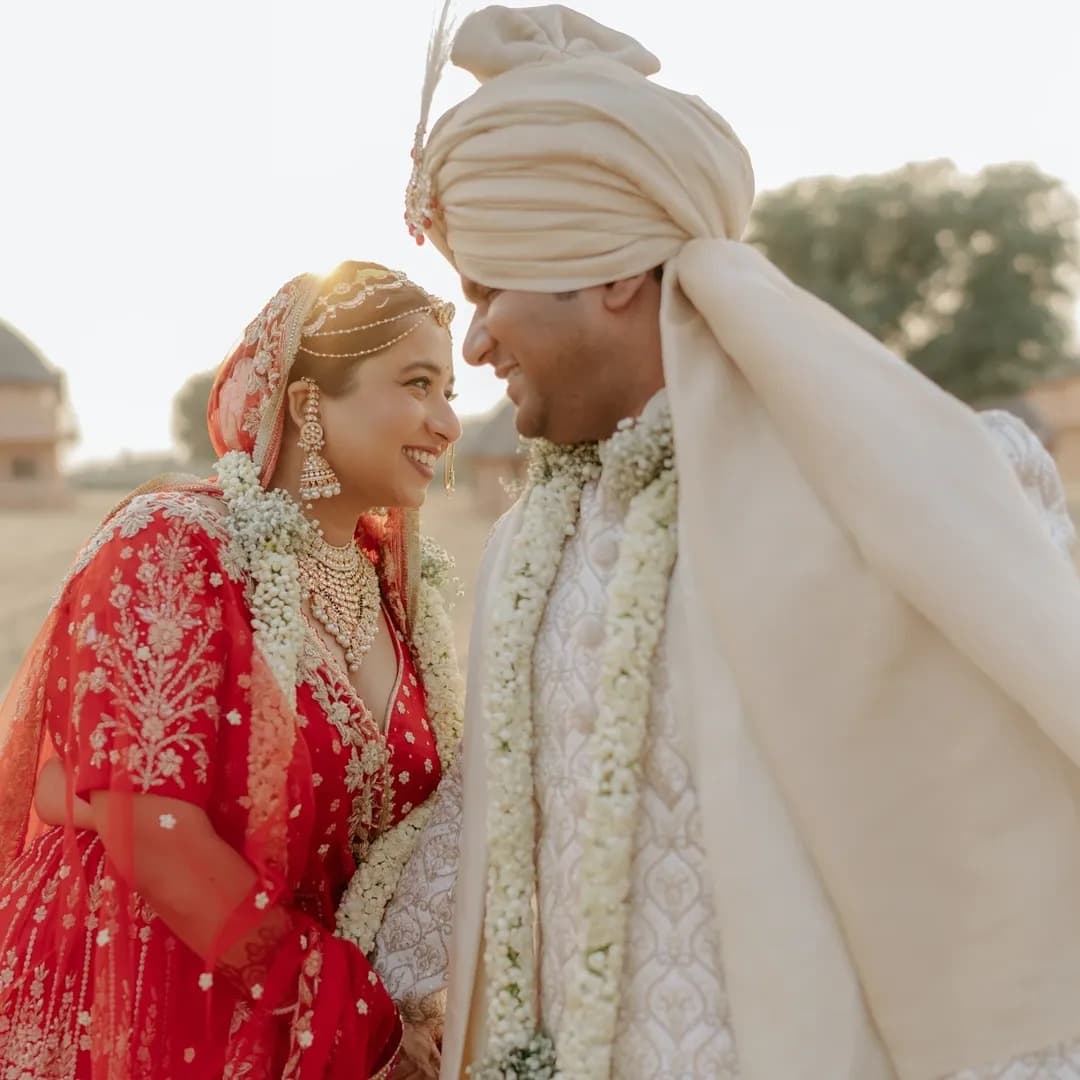 An Indian bride and groom in traditional wedding attire smiling face to face