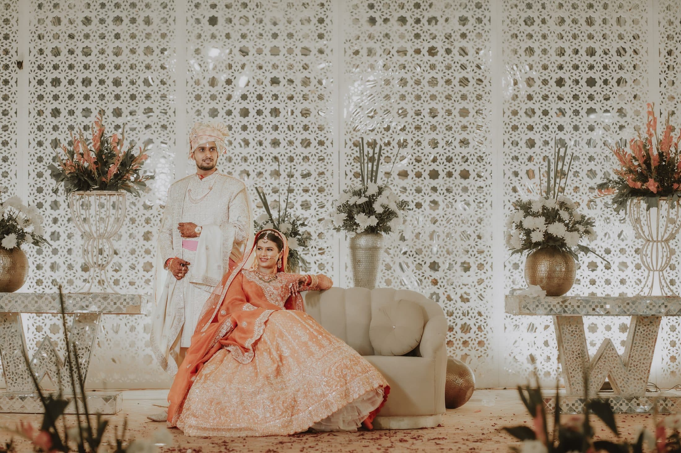 The bride seated beside the groom in front of a jali screen